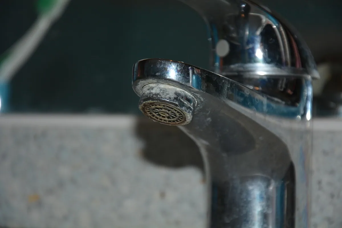 Grifo de lavabo con cal acumulada en el aireador y en la boca del caño