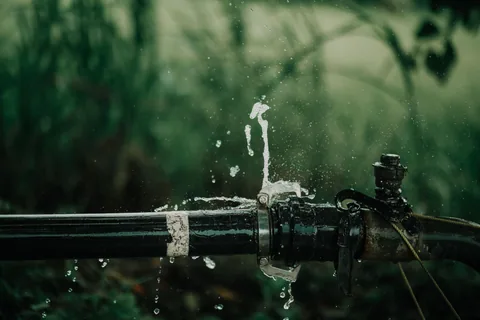 Agua saliendo a presión por la junta de una tubería rota, una urgencia de fontanería