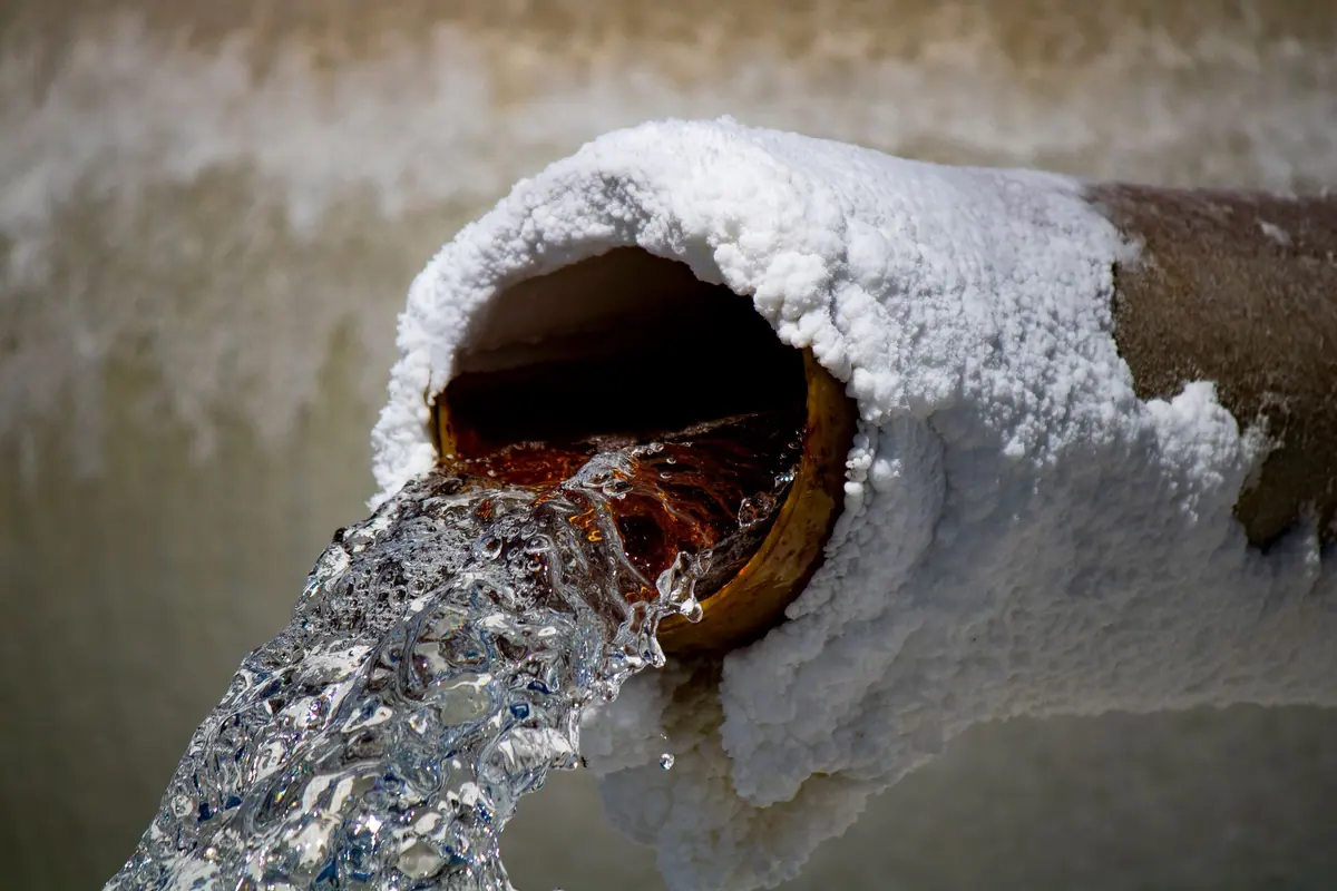 Chorro de agua saliendo de una tubería vieja, oxidada por dentro y cubierta por fuera de una costra blanca de sales