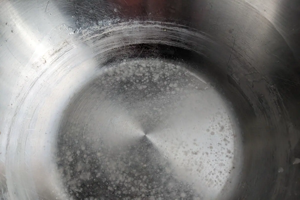Restos blancos de cal en el fondo de un cazo de acero inoxidable, como los que se forman al calentar el agua
