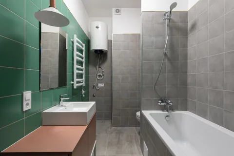 Termo eléctrico blanco instalado en la pared de un baño alicatado, con sus tomas de agua a la vista