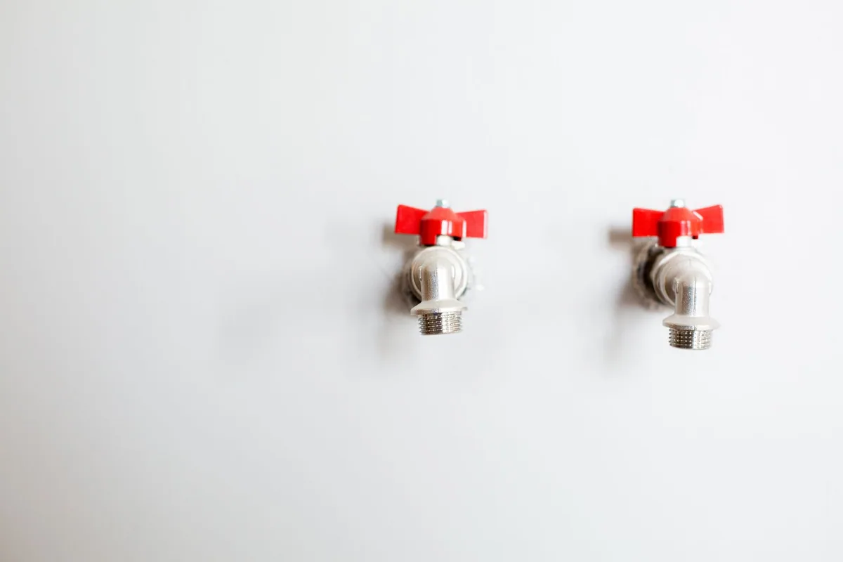 Dos llaves de toma de agua con maneta roja preparadas en una pared blanca para conectar aparatos