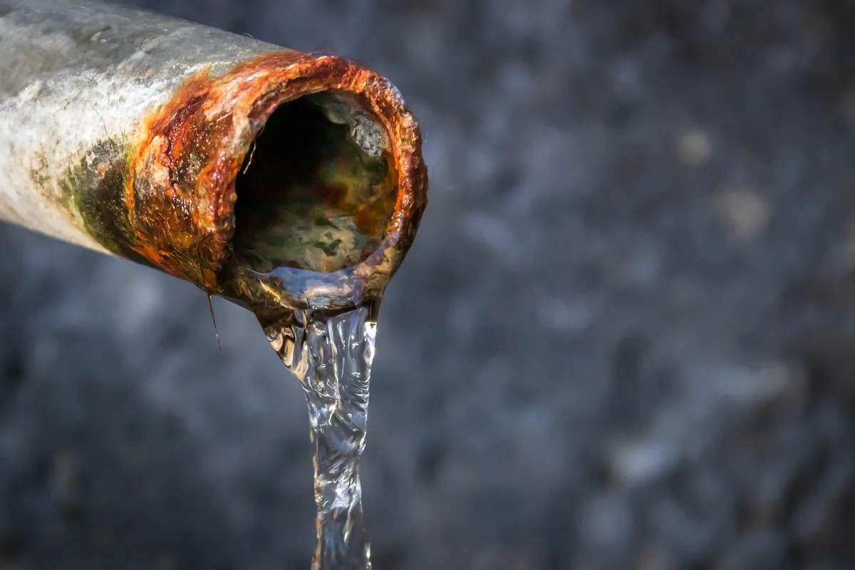 Tubería metálica antigua oxidada por fuera y por dentro, con agua saliendo por su extremo