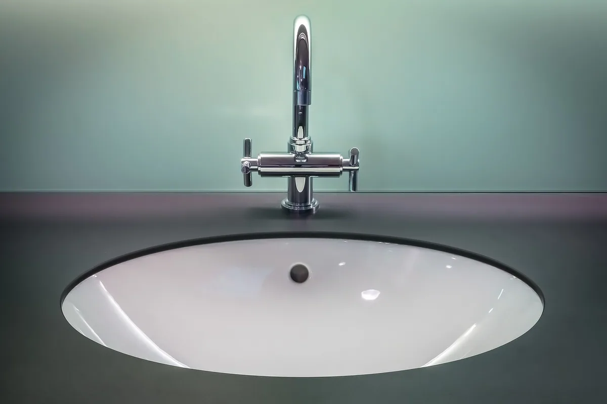 Grifo mezclador cromado de dos manetas sobre un lavabo blanco encastrado en una encimera oscura