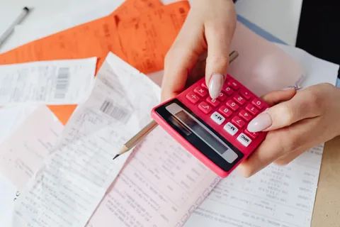 Manos con una calculadora roja sobre tiques y facturas, haciendo cuentas del precio de un fontanero